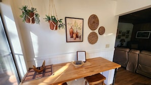 Une table de salle à manger en bois, agrémentée d’un set de table, de deux tabourets en bois et de pots de fleurs suspendus en macramé.