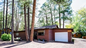 Une cabane avec un garage, entourée de grands arbres.