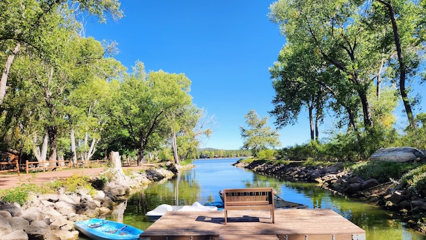 A wooden dock extending into a calm river, surrounded by lush greenery and trees. - Pines Cabin at The Lazy Oaks Resort (Lakeside)