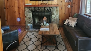 Una sala de estar acogedora con chimenea de piedra, un televisor de pantalla plana montado encima y un sofá de cuero, además de una alfombra estampada.