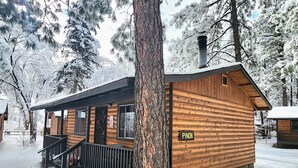 Una cabaña de madera con un porche, un letrero que dice "PINON" y una chimenea.
