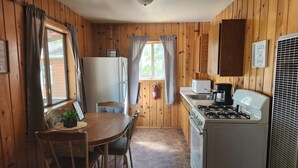 Una cocina compacta con paredes de madera, una mesa de comedor con sillas, un refrigerador, una estufa y un microondas.