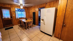 Una habitación con paneles de madera, una mesa de comedor, sillas, un refrigerador y un ventilador de techo.
