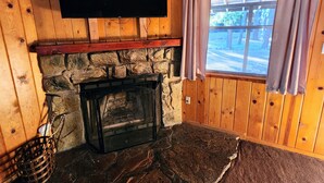 Una habitación acogedora con chimenea de piedra, paredes de madera y una ventana con cortinas.