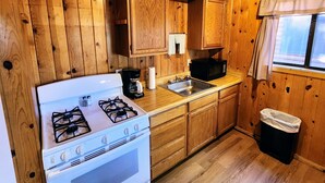 A compact kitchen with wooden cabinets, a white stove, a microwave, and a sink. - Poplars Cabin at Lazy Oaks Resort (Lakeside)