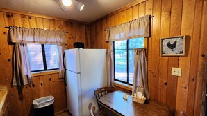 A wooden cabin interior with a refrigerator, dining table, chairs, and a trash bin. - Poplars Cabin at Lazy Oaks Resort (Lakeside)