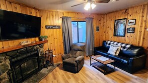 A cozy living room with a fireplace, a television, a sofa, and a ceiling fan. - Poplars Cabin at Lazy Oaks Resort (Lakeside)
