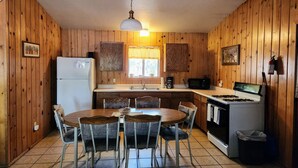 Una cocina con paredes de madera, un refrigerador blanco, una estufa, un microondas y una mesa de comedor con sillas.