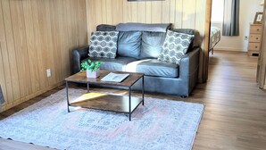 A cozy living room with a leather sofa, a coffee table, and a rug. - Willows Cabin at Lazy Oaks Resort (Lakeside)
