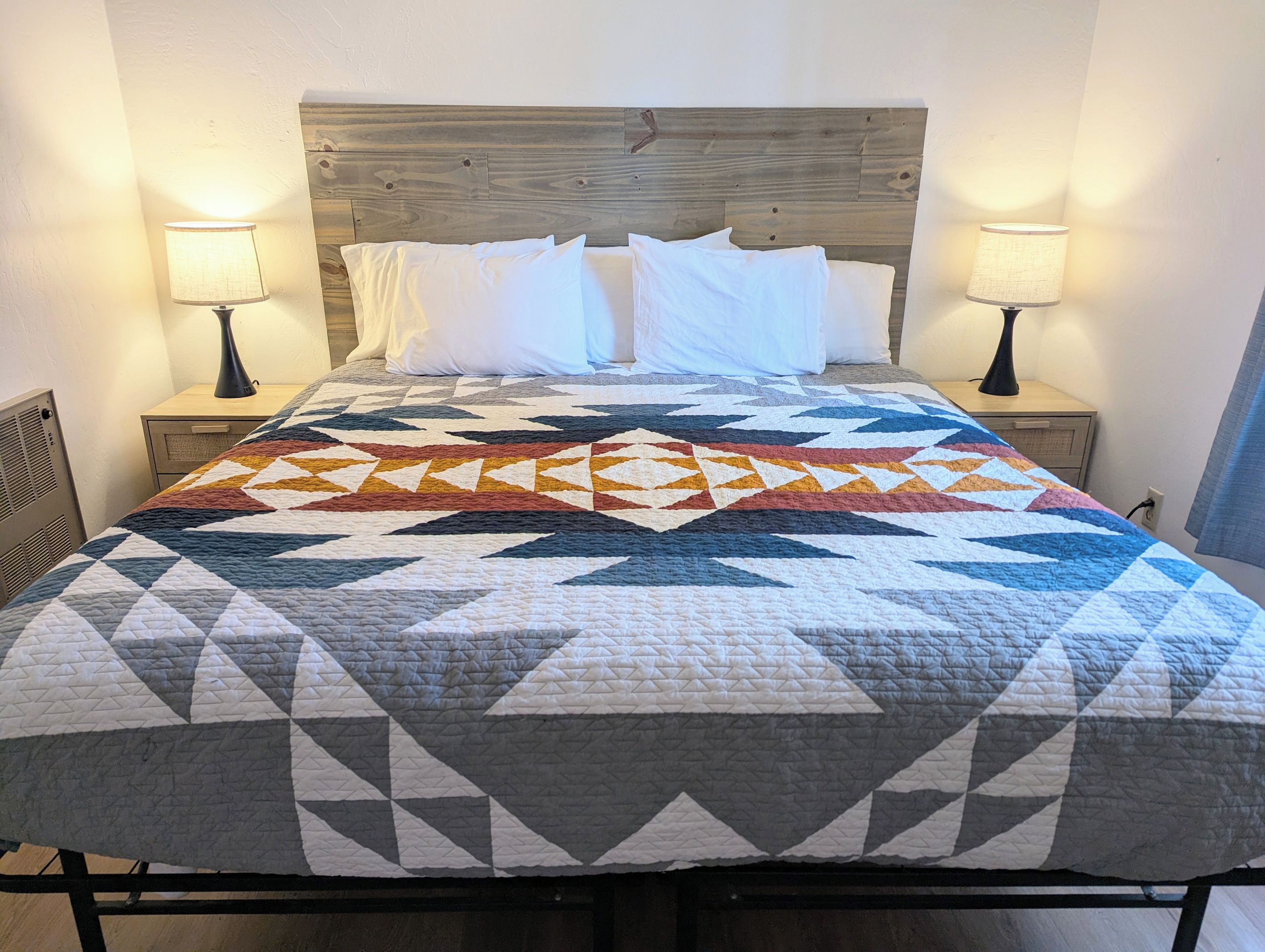 A bed with a geometric patterned quilt, two bedside lamps, and a wooden headboard.
