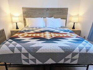 A bed with a geometric patterned quilt, two bedside lamps, and a wooden headboard. - Willows Cabin at Lazy Oaks Resort (Lakeside)