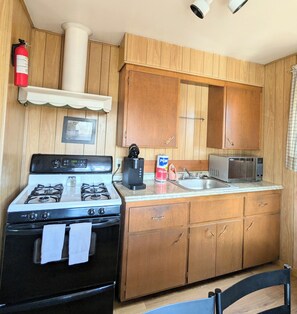 A compact kitchen with a gas stove, a microwave, wooden cabinets, and a small sink.