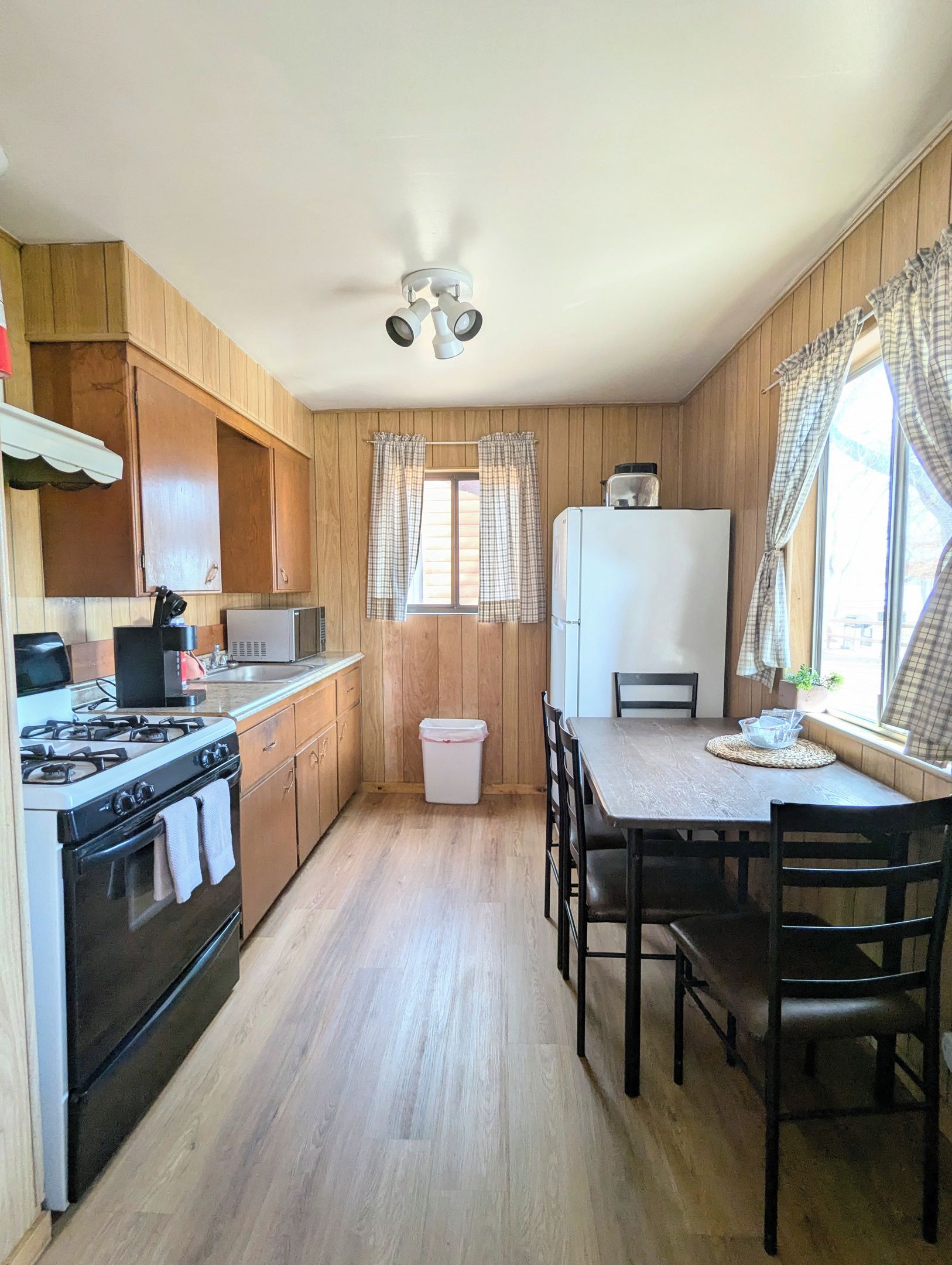 A kitchen with wooden paneling, a gas stove, a microwave, a refrigerator, and a dining table with chairs.
