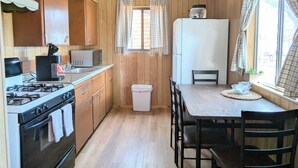 A kitchen with wooden paneling, a gas stove, a microwave, a refrigerator, and a dining table with chairs. - Willows Cabin at Lazy Oaks Resort (Lakeside)