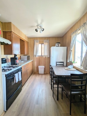 A kitchen with wooden paneling, a gas stove, a microwave, a refrigerator, and a dining table with chairs. - Willows Cabin at Lazy Oaks Resort (Lakeside)