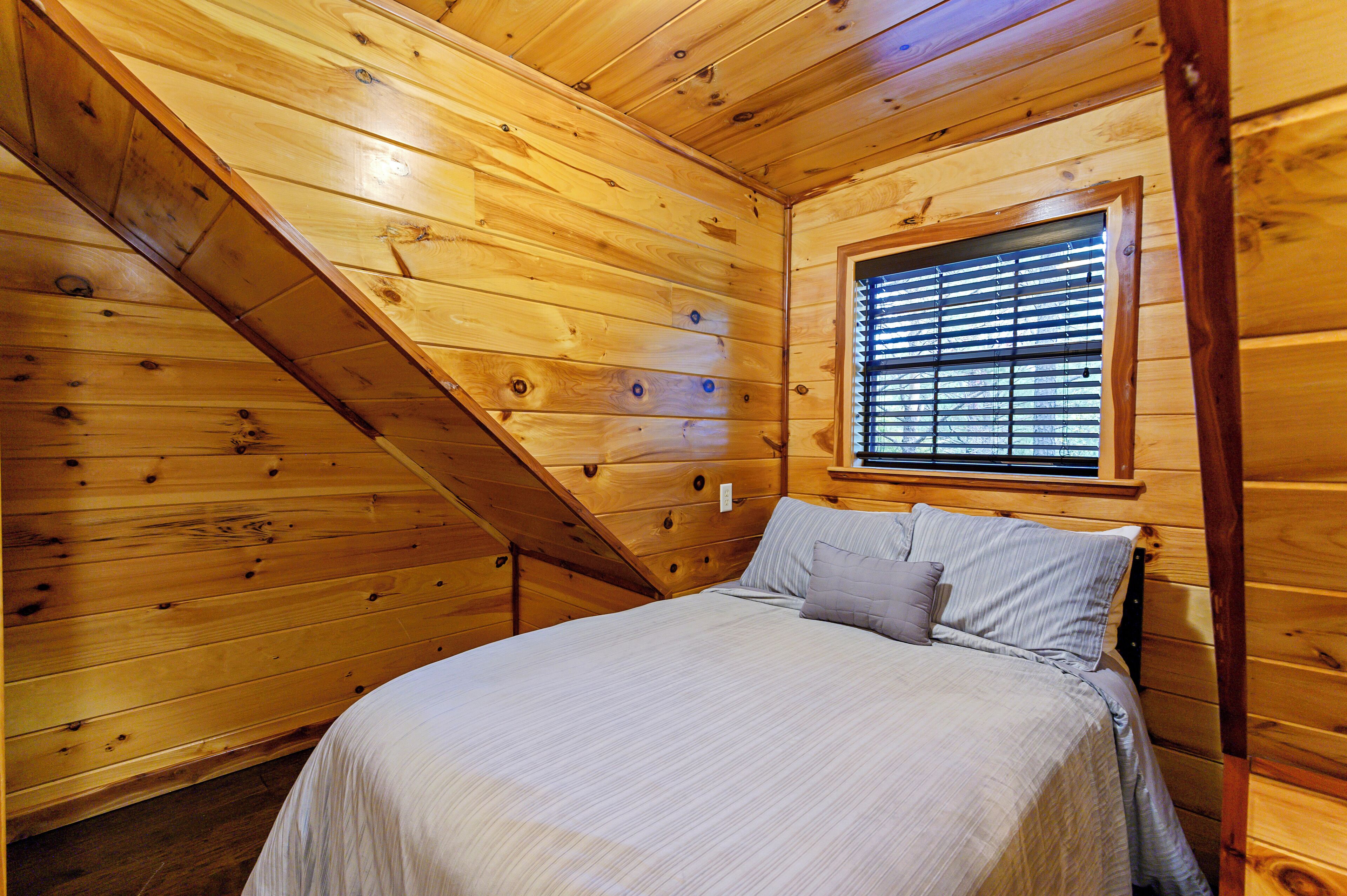 A wooden cabin bedroom with a bed, window blinds, and a sloped ceiling.