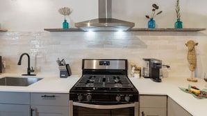 A modern kitchen with a gas stove, oven, and stainless steel range hood. There are two blue vases with dried flowers on a shelf above the stove. - Maldives Vibe | Ping-Pong | Firepit I Yoga (Austin)