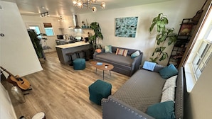 A modern living room with a grey sectional sofa, a small coffee table, and a dining area with a kitchen in the background. - Maldives Vibe | Ping-Pong | Firepit I Yoga (Austin)