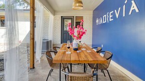 A wooden dining table with chairs, a vase with pink flowers, and a wall with the text "MADEVÍA". - Santorini Inspired | Firepit | Grill I Yoga (Austin)