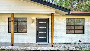 A modern house with a white brick exterior, a black front door, and two windows on either side. - Santorini Inspired | Firepit | Grill I Yoga (Austin)