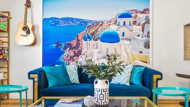 A living room with a blue sofa, a glass coffee table, and a painting of a coastal scene. - Fun Group Travel Retreat (Austin)