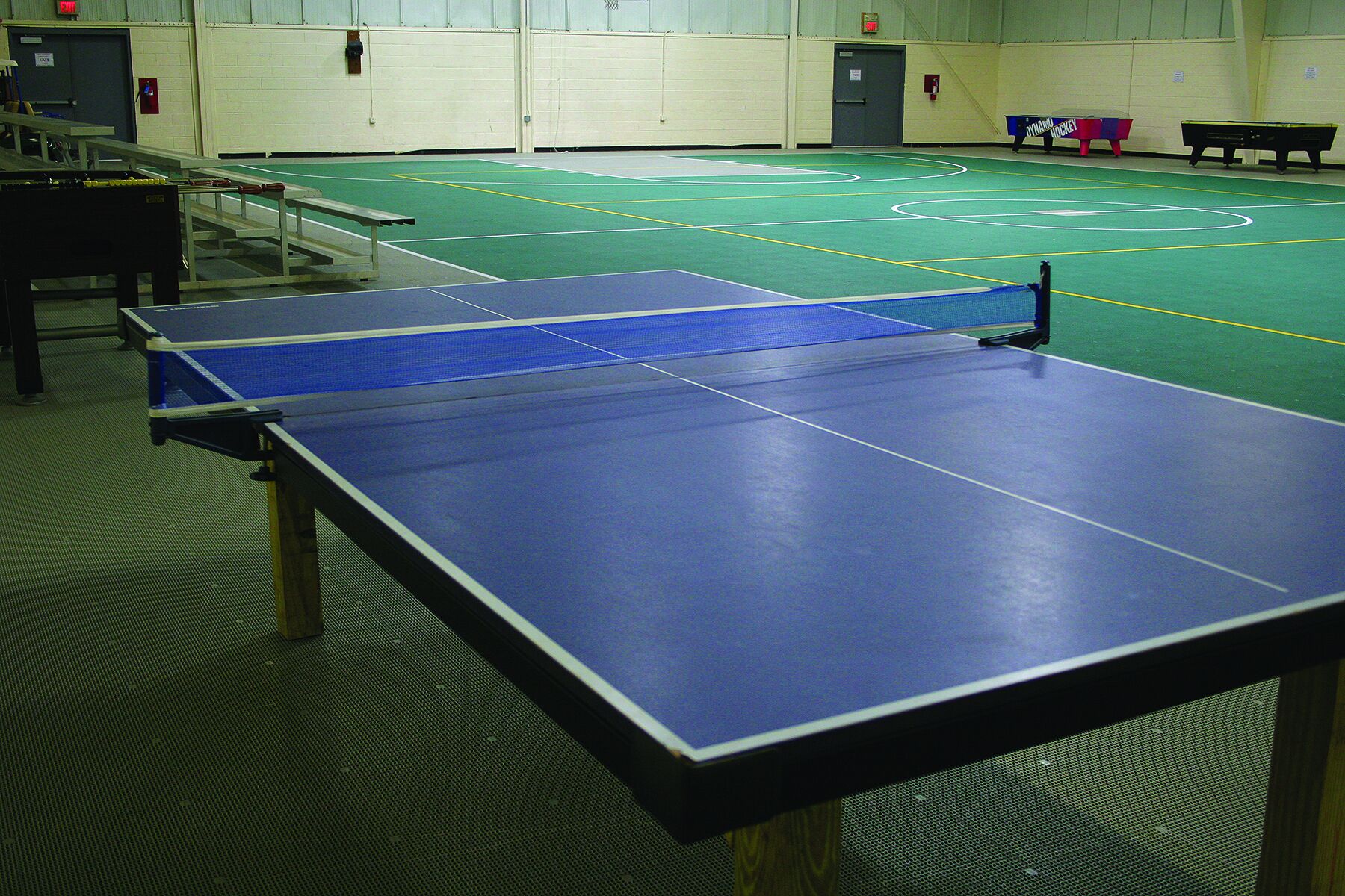 A table tennis court with multiple tables and a basketball court in the background.