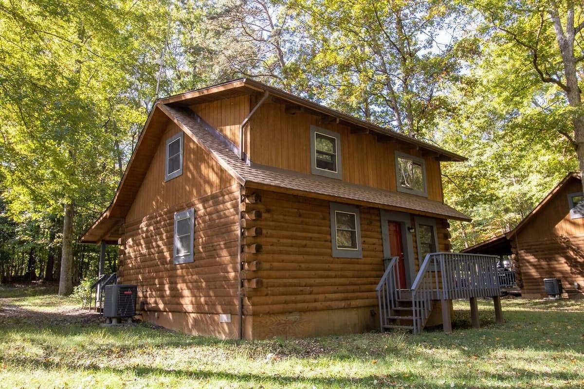 A two-story log cabin with a front porch and a small staircase leading to the entrance.
