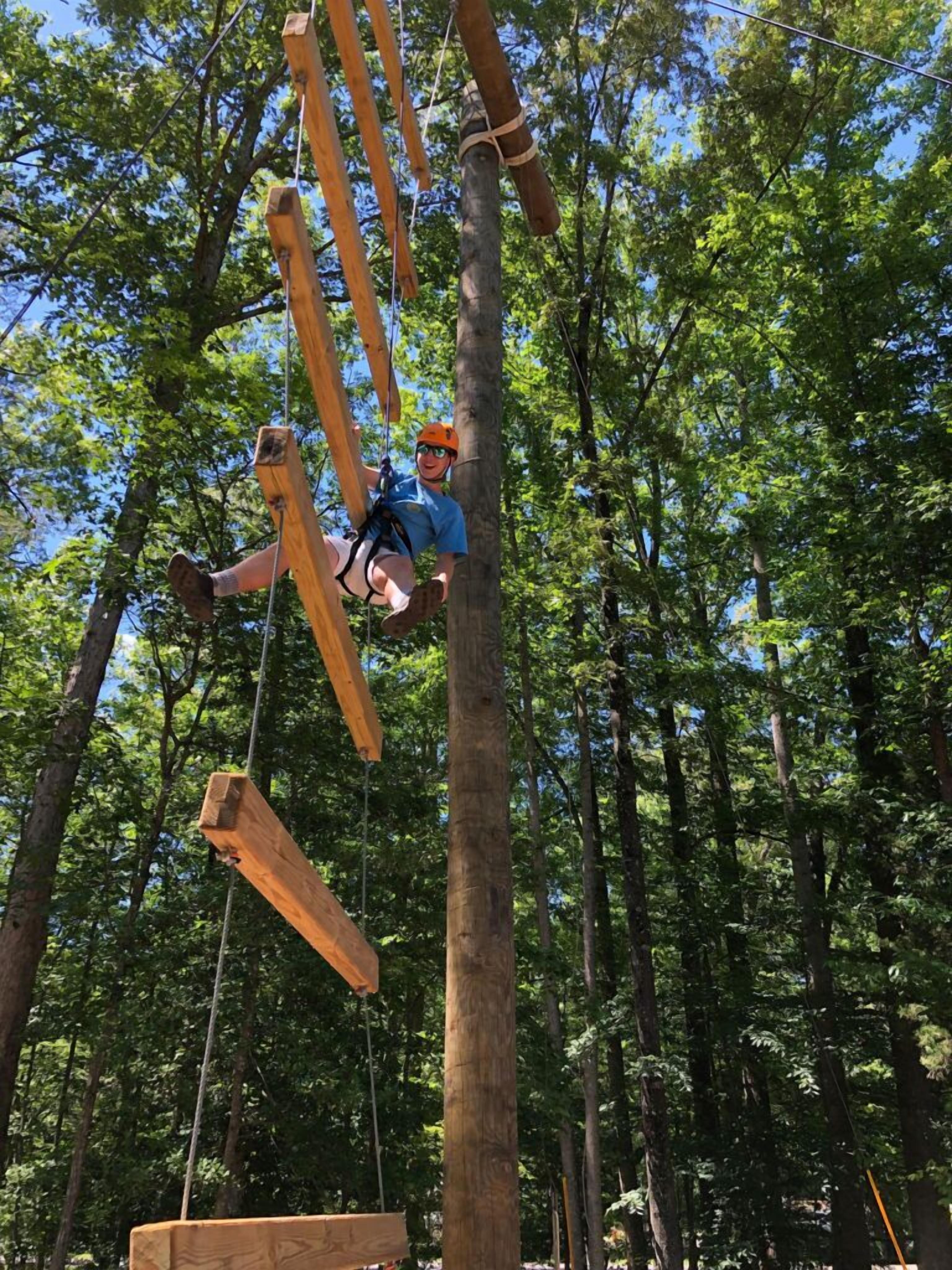 Una persona suspendida en un bosque, utilizando una estructura de madera para escalar.