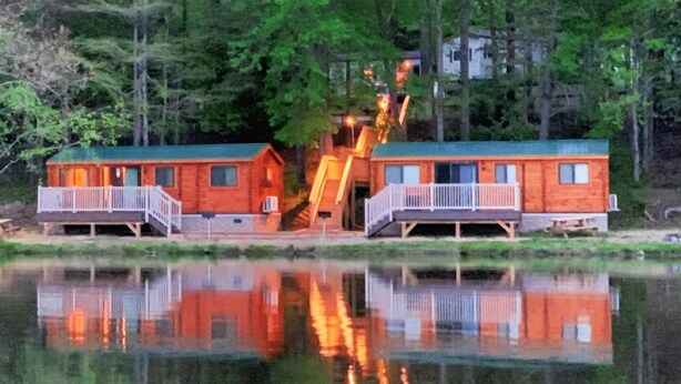 Two wooden cabins with balconies, a dock, and a reflection in the water. - Wilderness Presidential Resort (Spotsylvania)