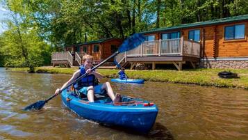 Una persona en un kayak azul en un río, con una cabaña al fondo.