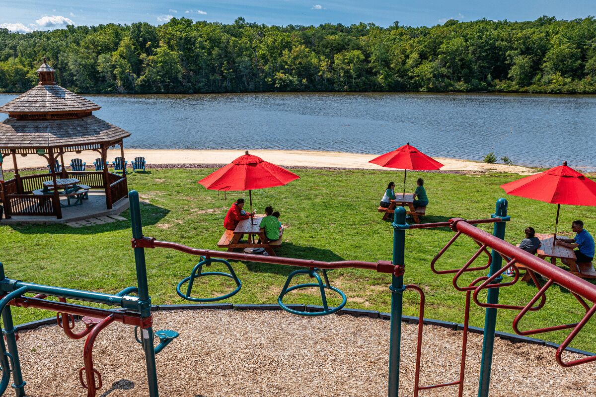 Un parque infantil con equipo de ejercicio y mesas de picnic junto a un lago.