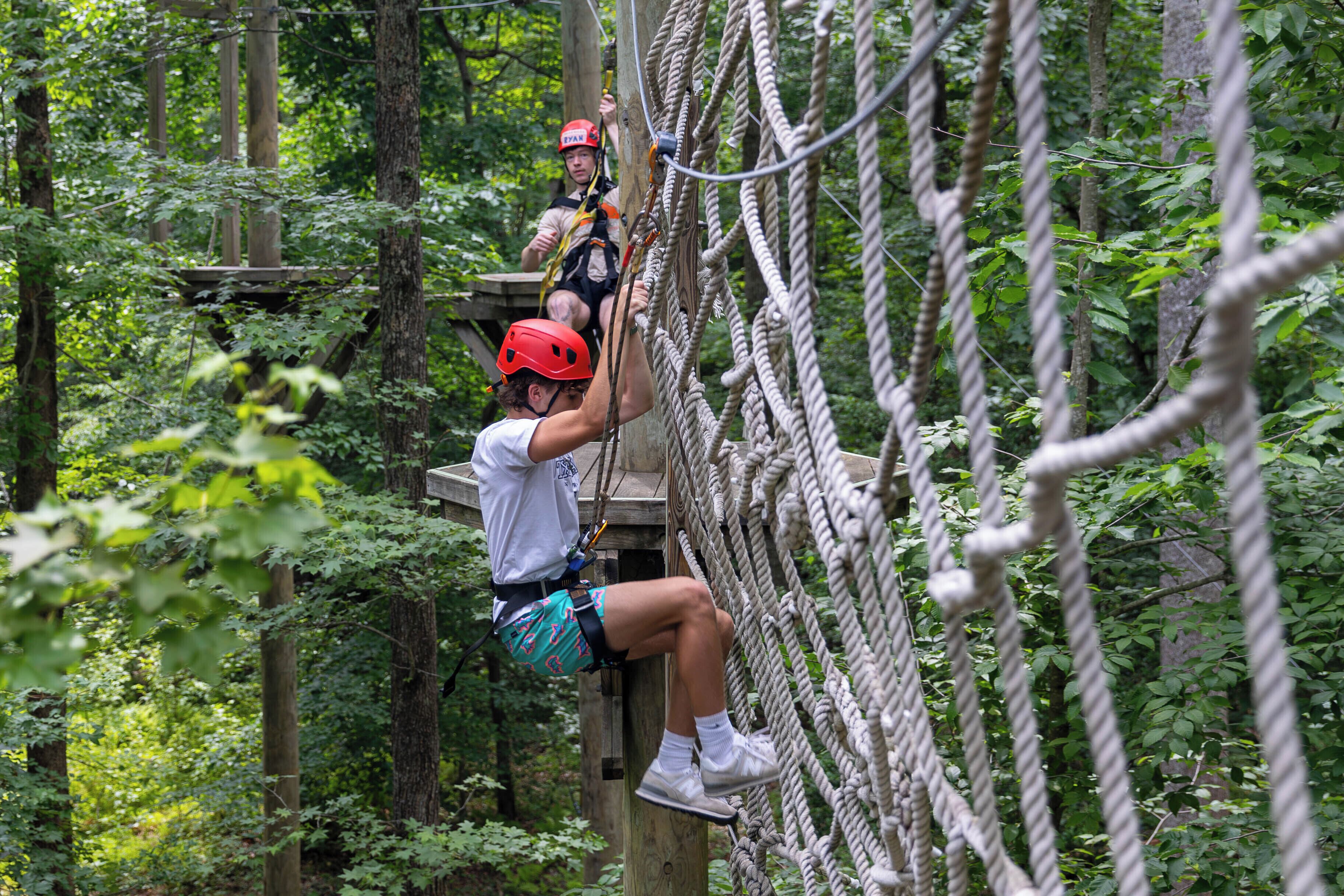 A person climbing a rope bridge in a forested area.