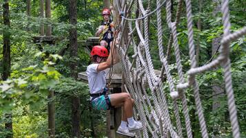 A person climbing a rope bridge in a forested area.