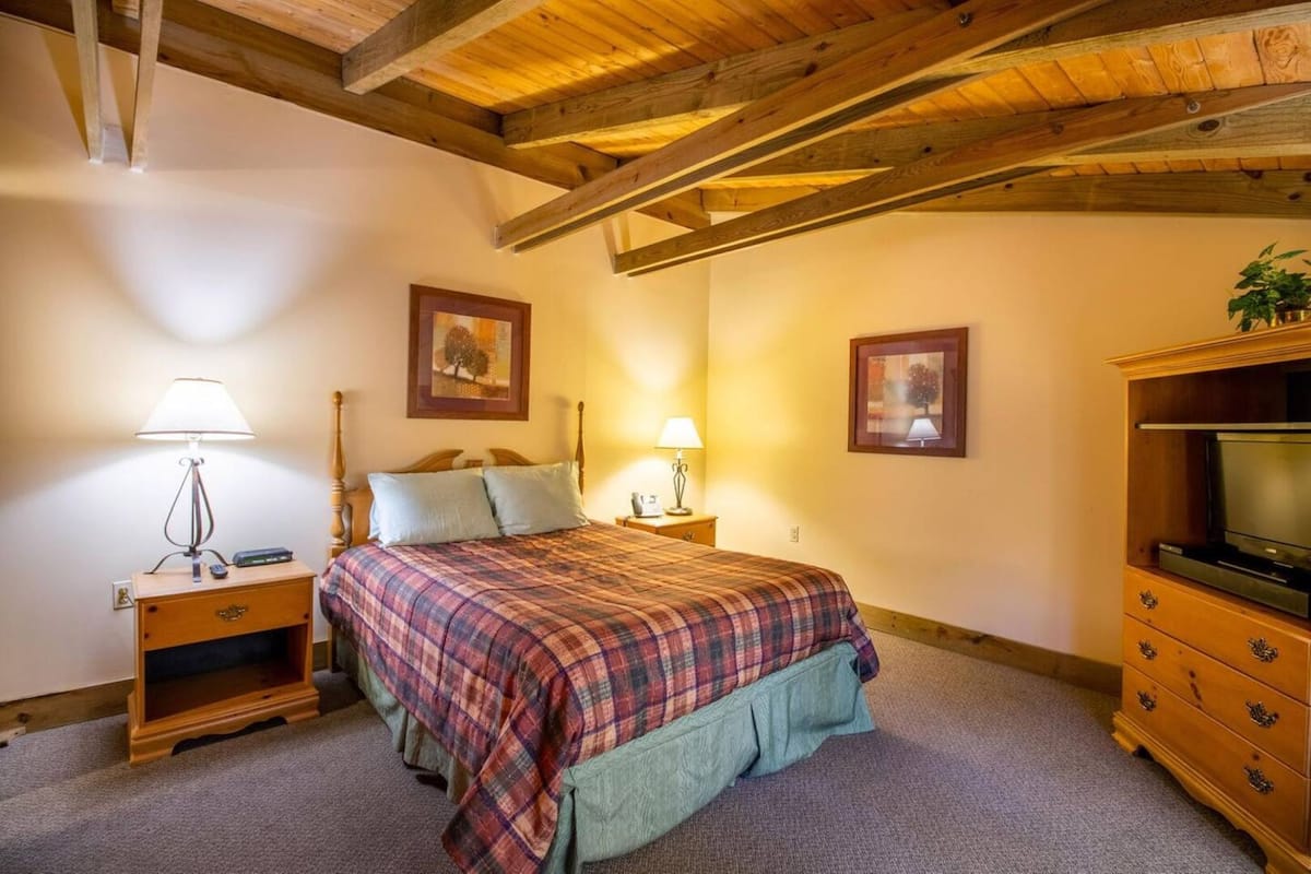 A bedroom with a bed, bedside lamps, a wooden dresser, and a television.