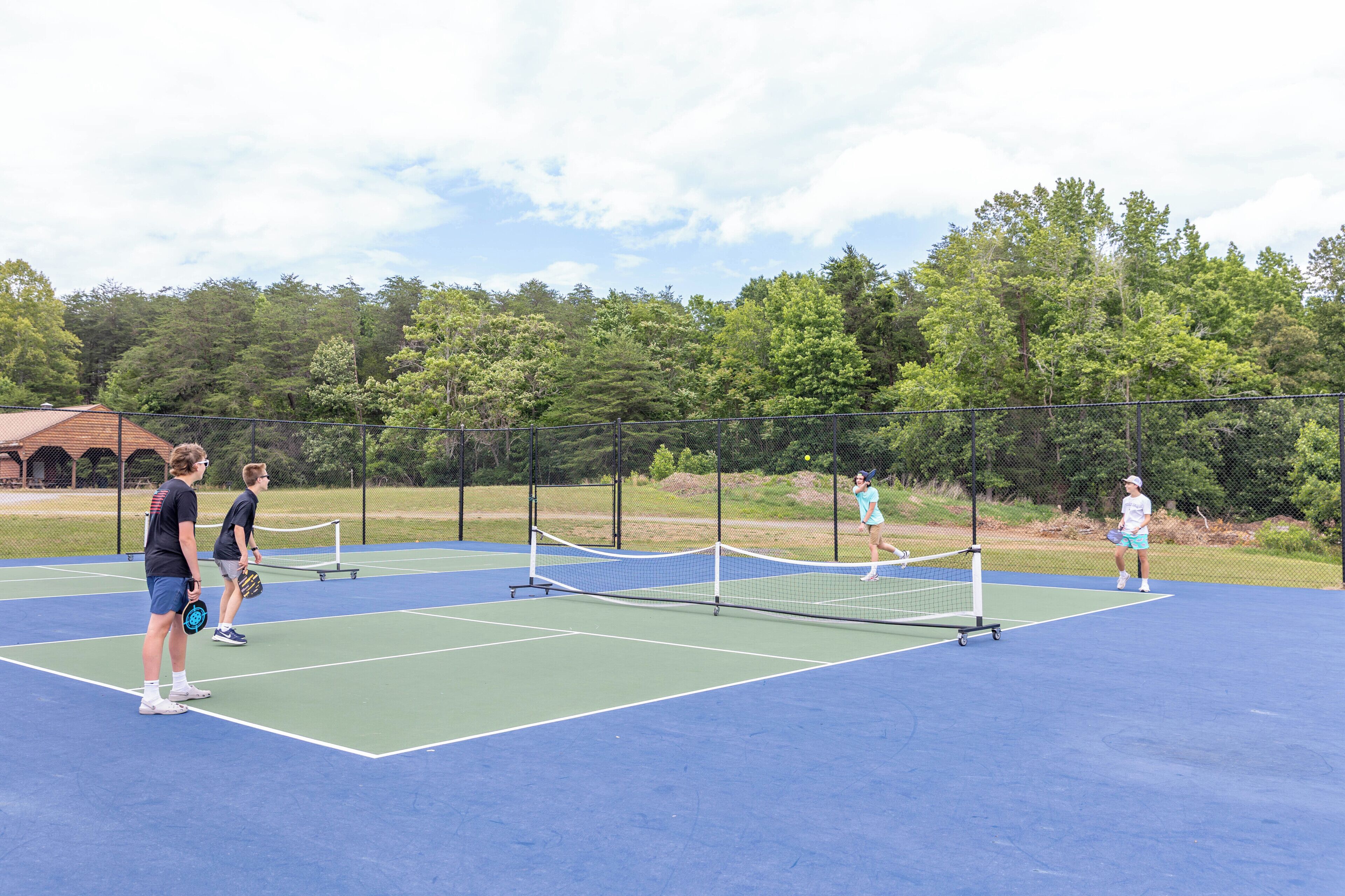 Ulkotenniskenttä, jossa on verkko, ja jonka ympärillä on metallinen aita sekä puita.
