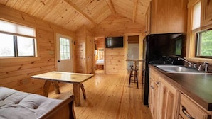 A wooden cabin interior with a dining table, kitchen area, and a bed. - Wilderness Presidential Resort (Spotsylvania)
