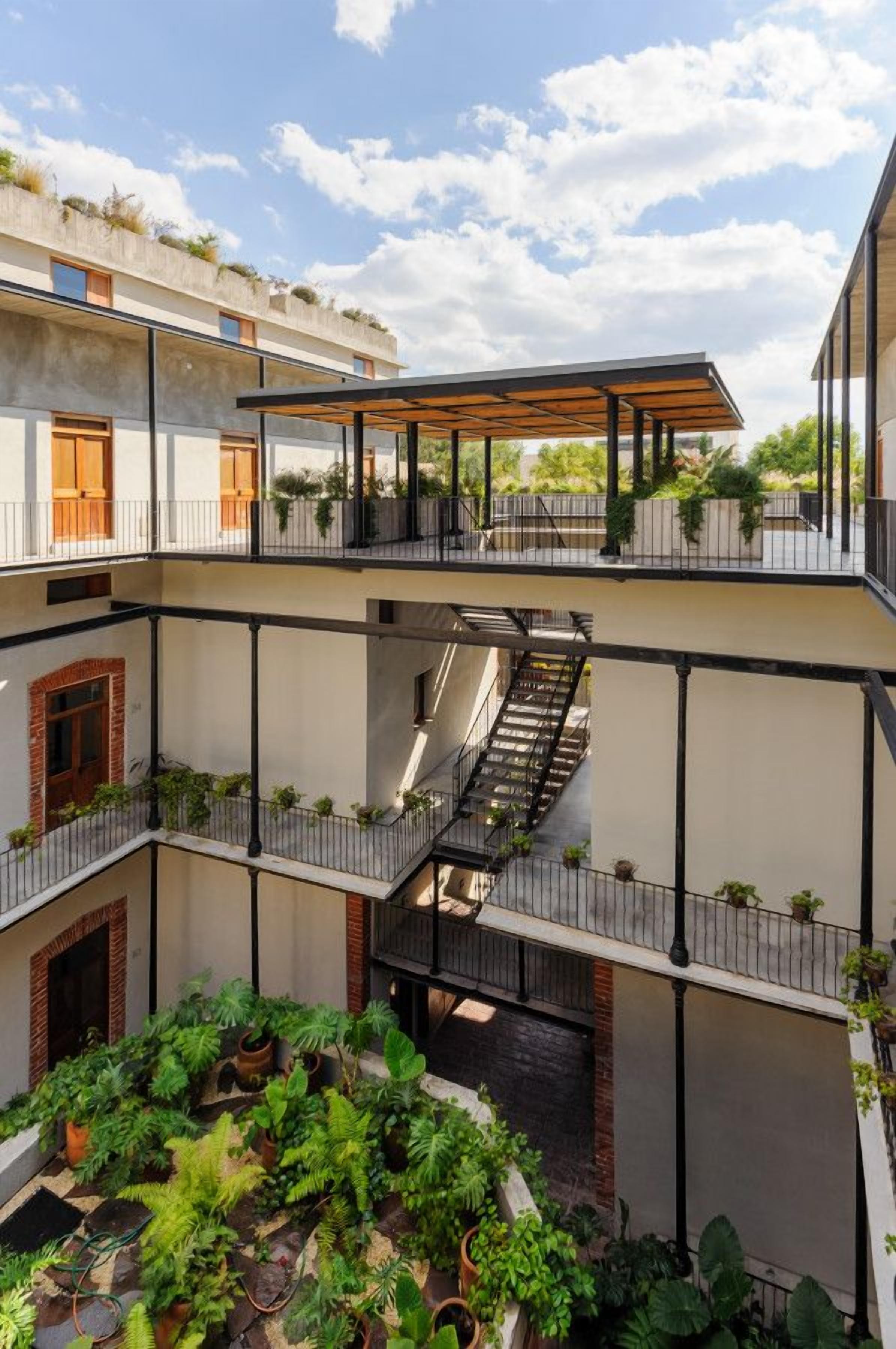Une cour intérieure à plusieurs niveaux, dotée d’un espace de repos abrité, d’un escalier et de plantes en pot.