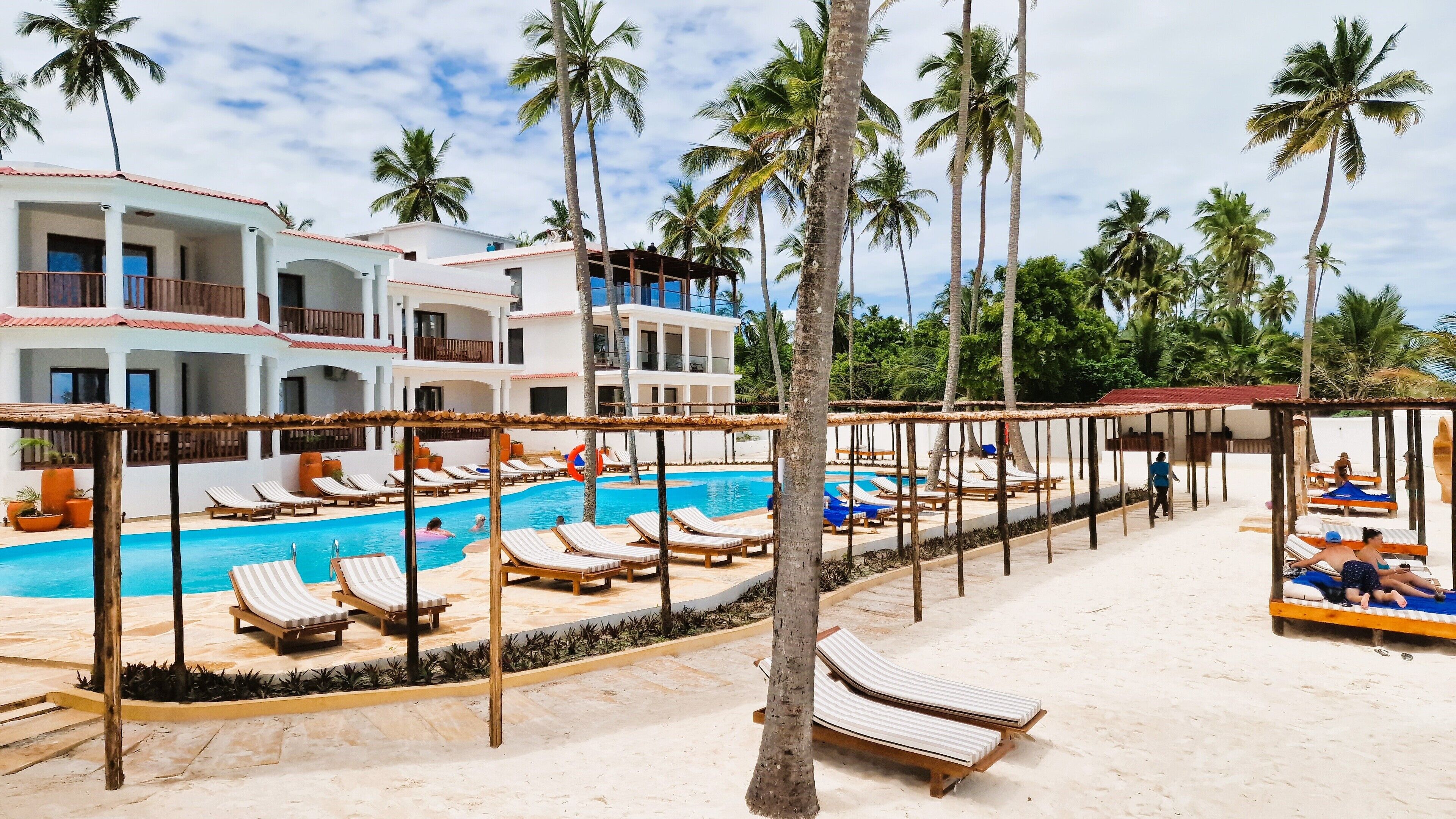 A resort with a swimming pool, sun loungers, and palm trees.