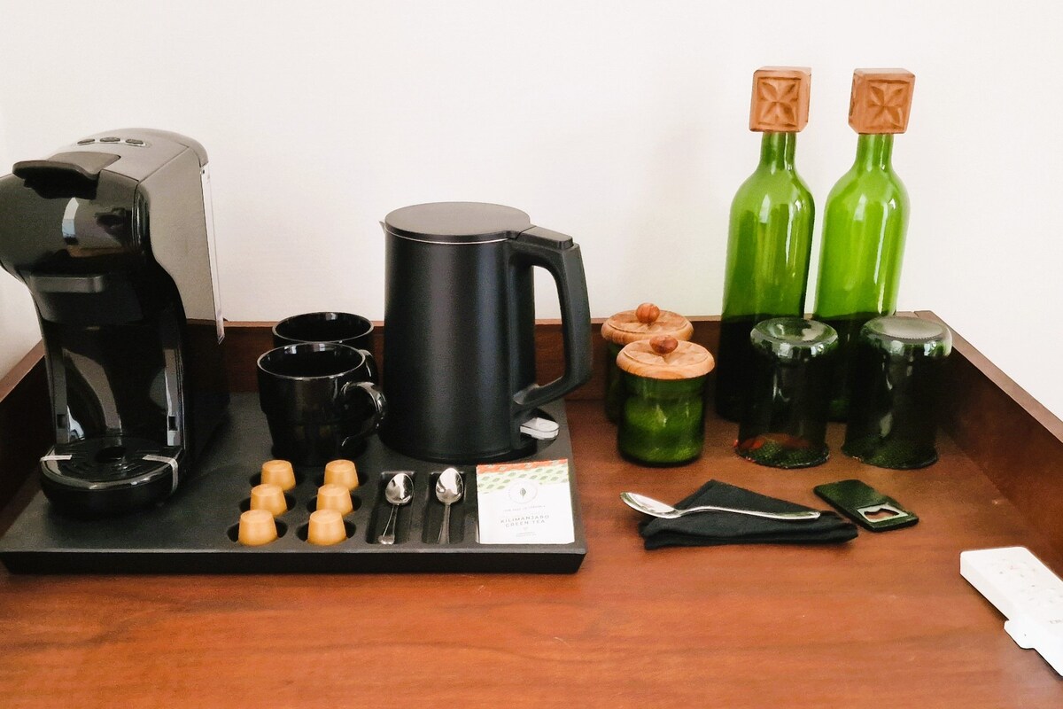 A coffee maker, a black coffee pot, two green bottles, and a tray with cups and spoons.