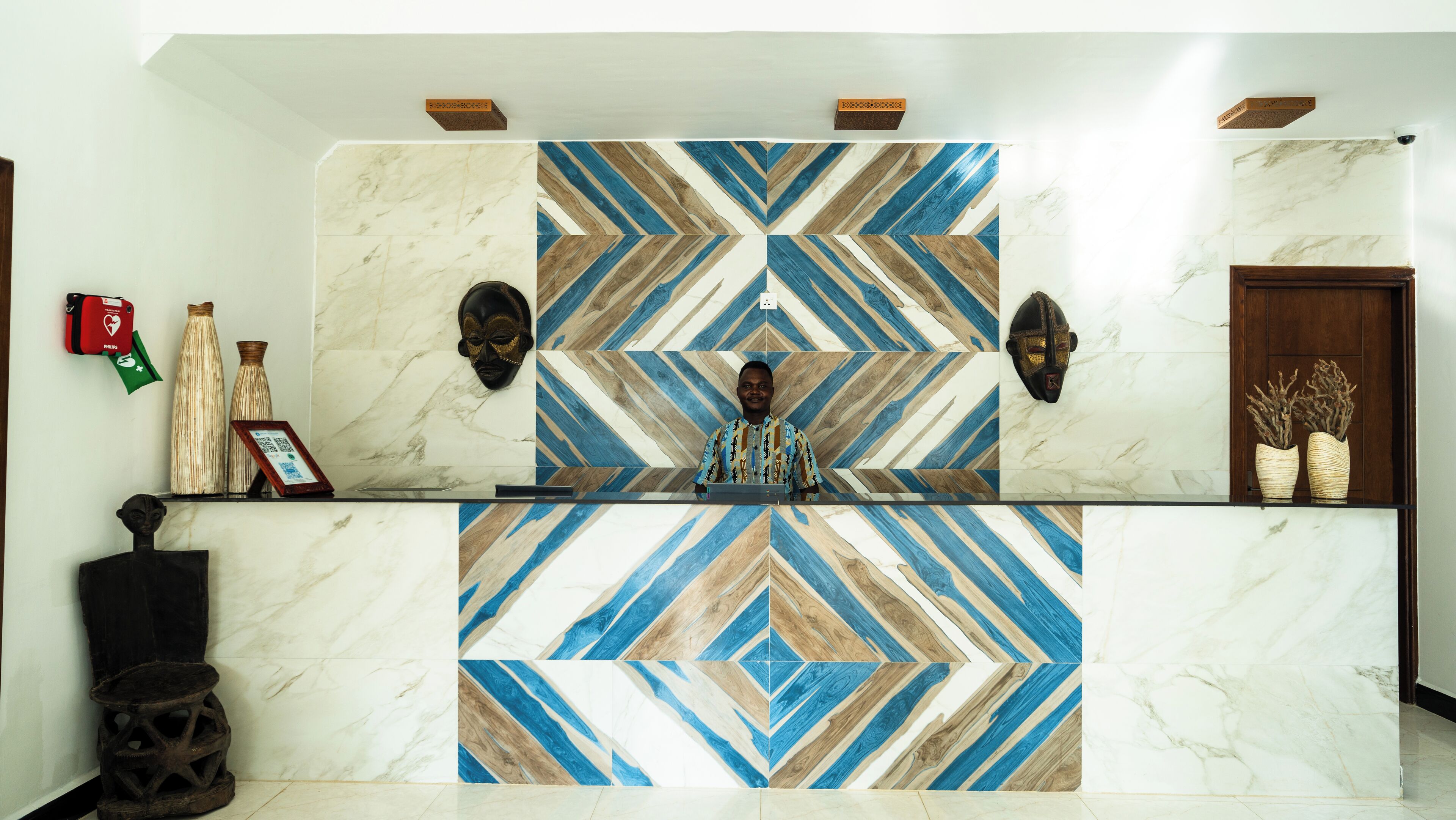 A reception desk with a geometric patterned tile design, two wall-mounted masks, and a wooden door.