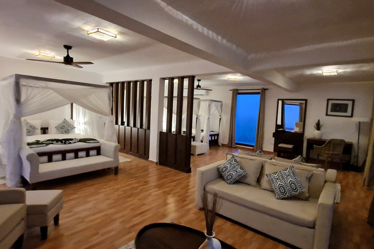A spacious room with a large bed, a sofa, and a balcony.