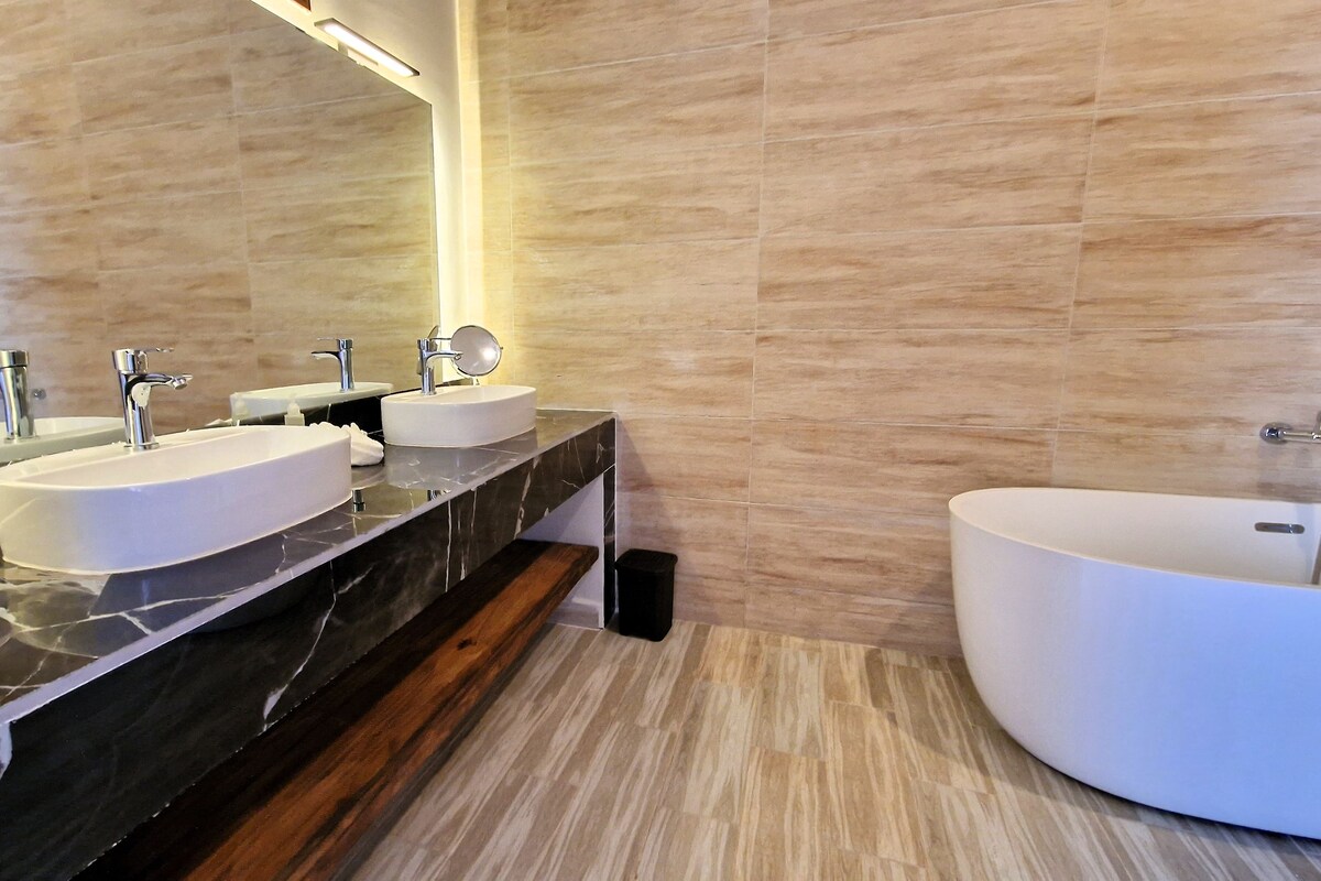 Une salle de bain moderne avec deux vasques, un grand miroir et une baignoire sur pieds.