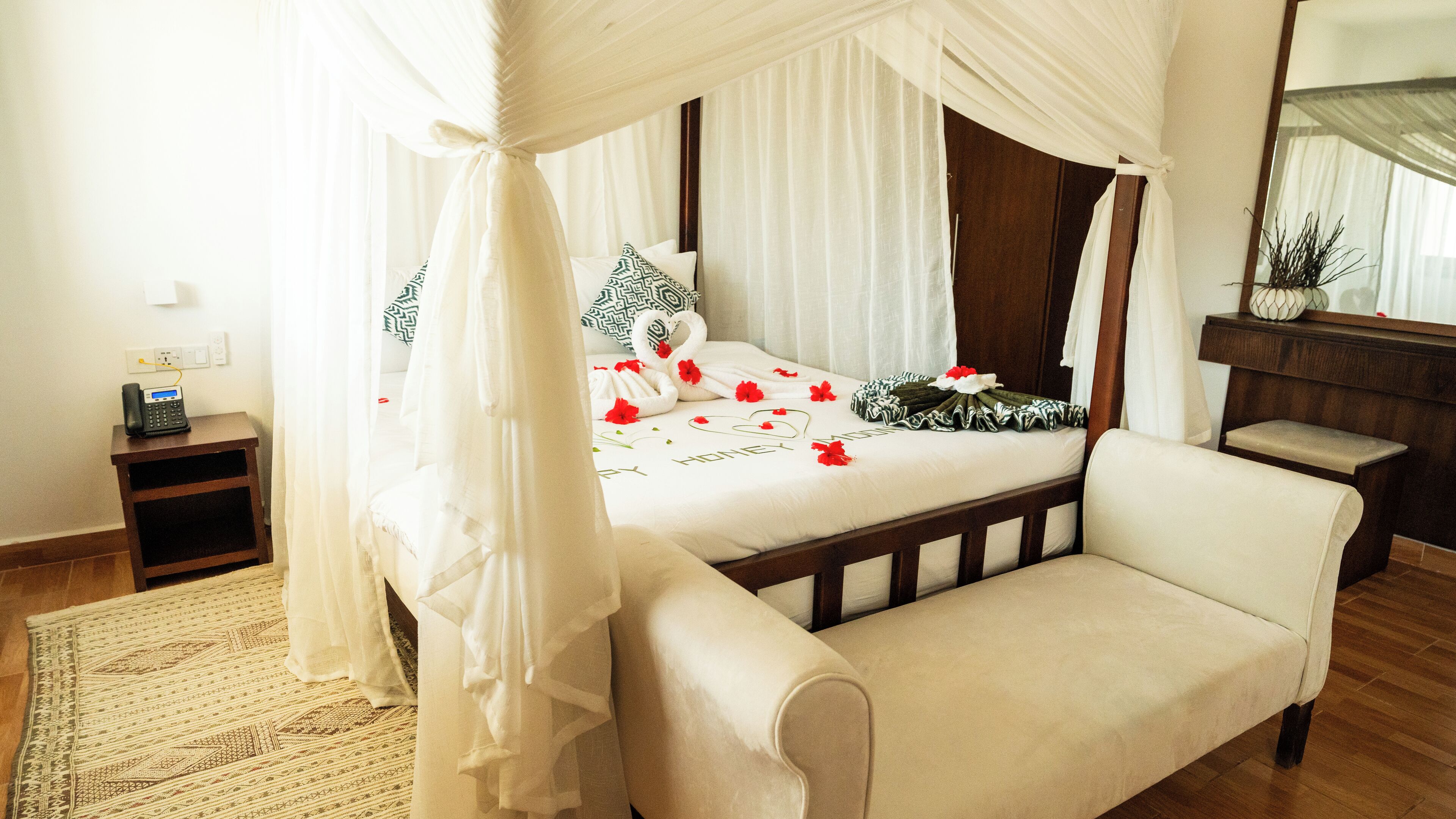 A bedroom with a four-poster canopy bed, a bedside table with a phone, a chair, and a bedside plant.