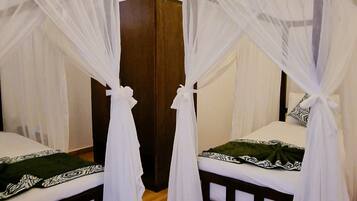 A room with two beds, each with a canopy. There is a wooden floor and a white wall with a light fixture.