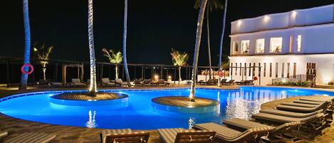 A nighttime pool area with lounge chairs and palm trees.