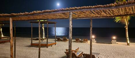 A beachside lounge with wooden chairs and a thatched roof structure, overlooking the ocean.