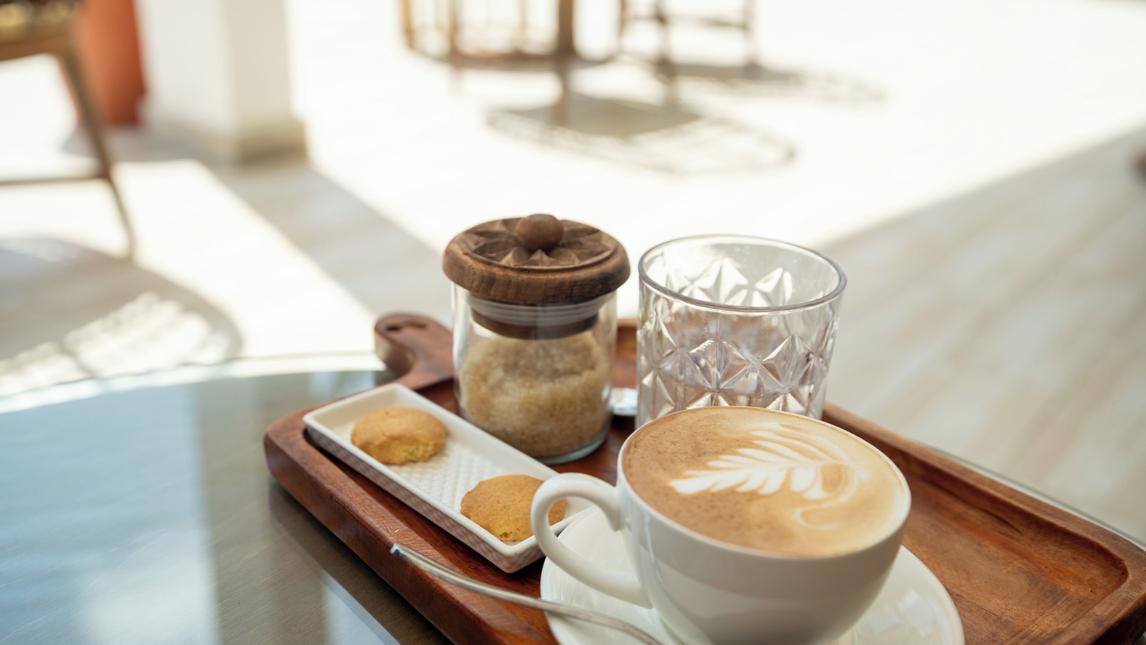 A tray with a cup of coffee, a glass, and a jar of sugar on a table.