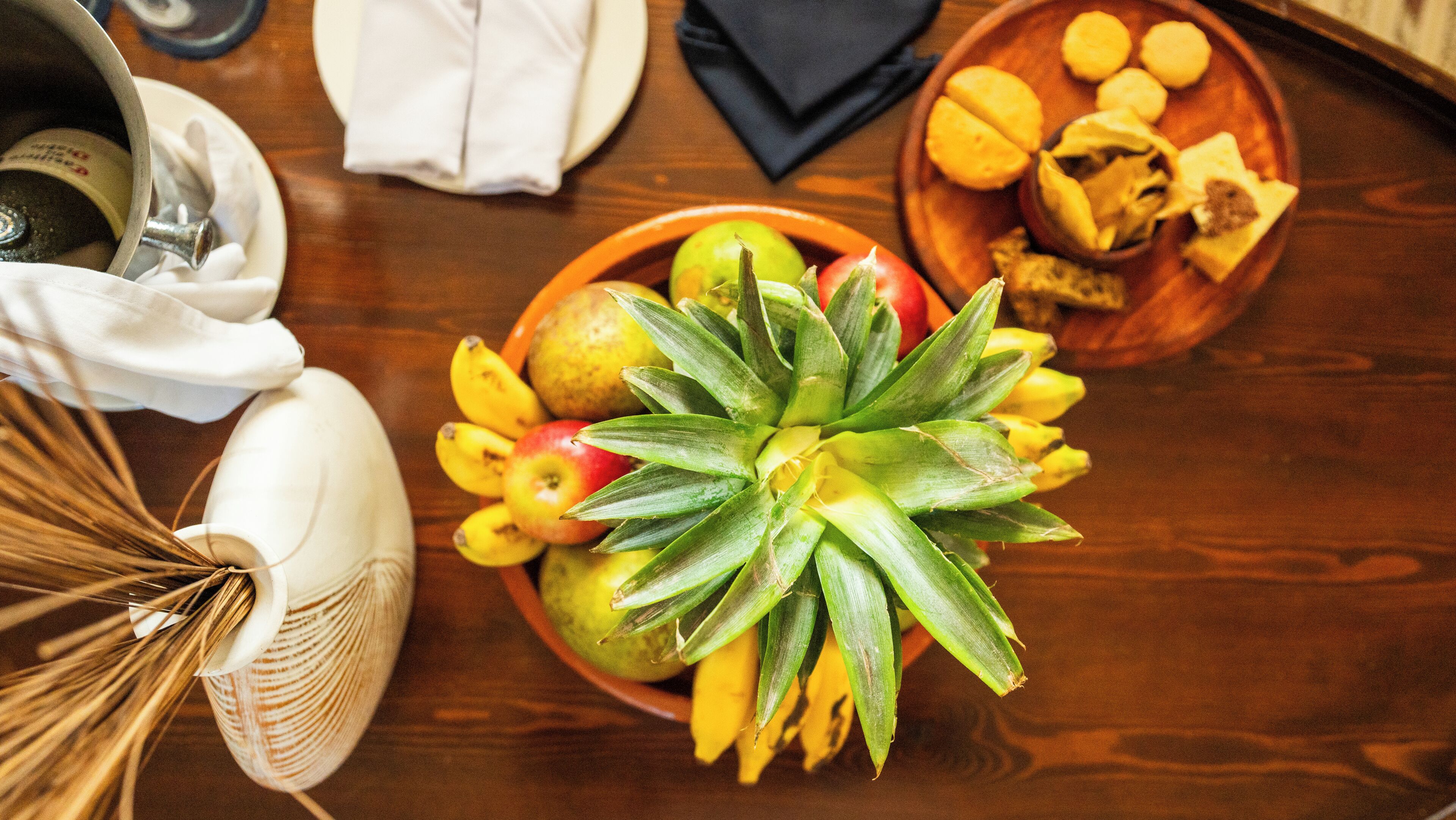 A wooden table with a bowl of fruit, a plate with food, and a bottle.