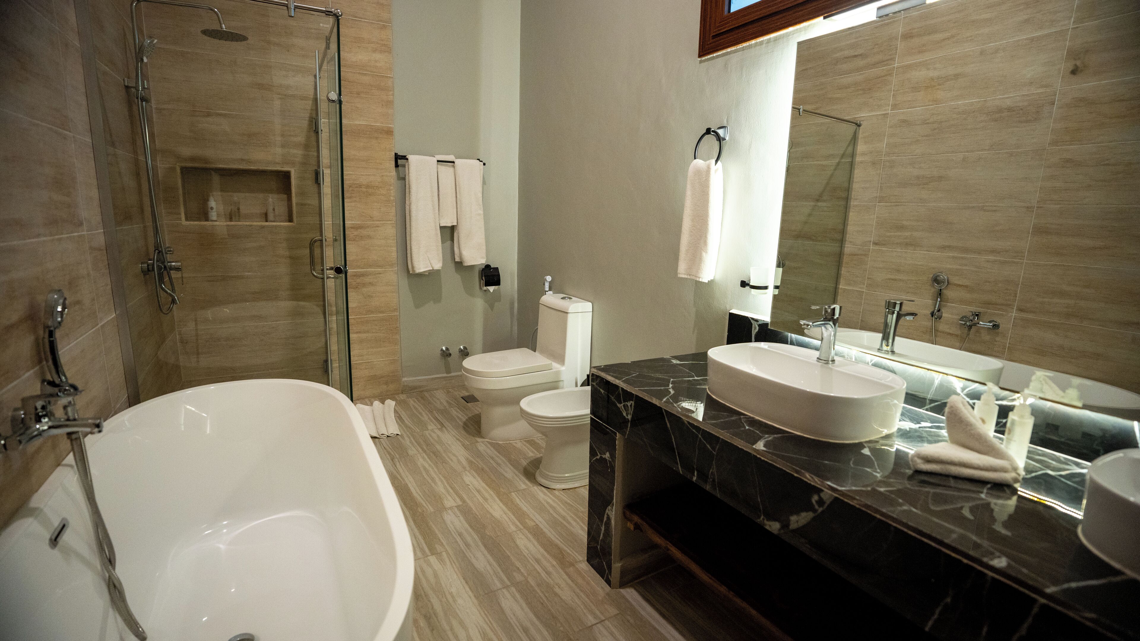 A modern bathroom with a freestanding bathtub, a toilet, and a sink with a large mirror above.