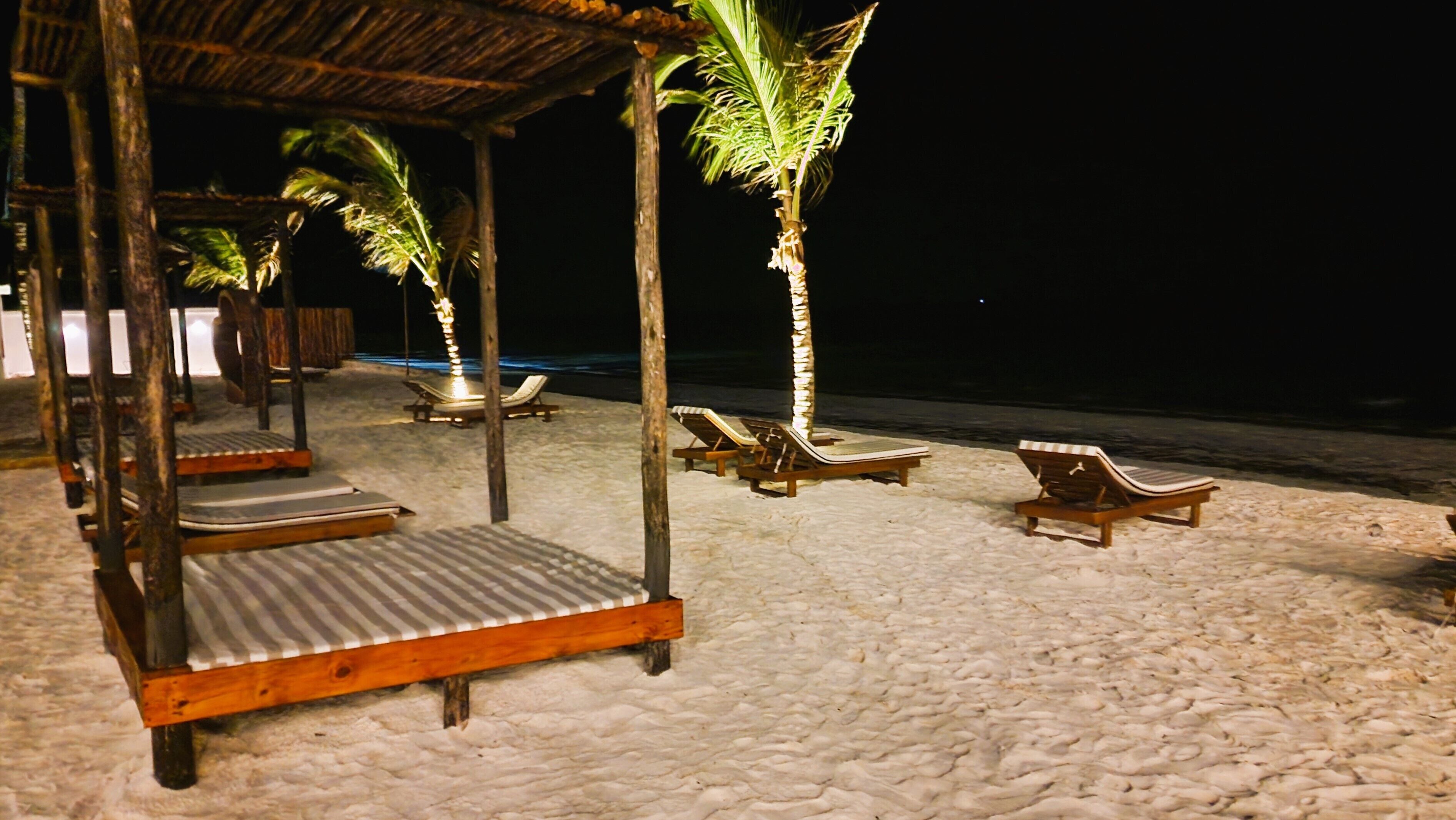 A beachside lounge with wooden loungers and a thatched roof structure.